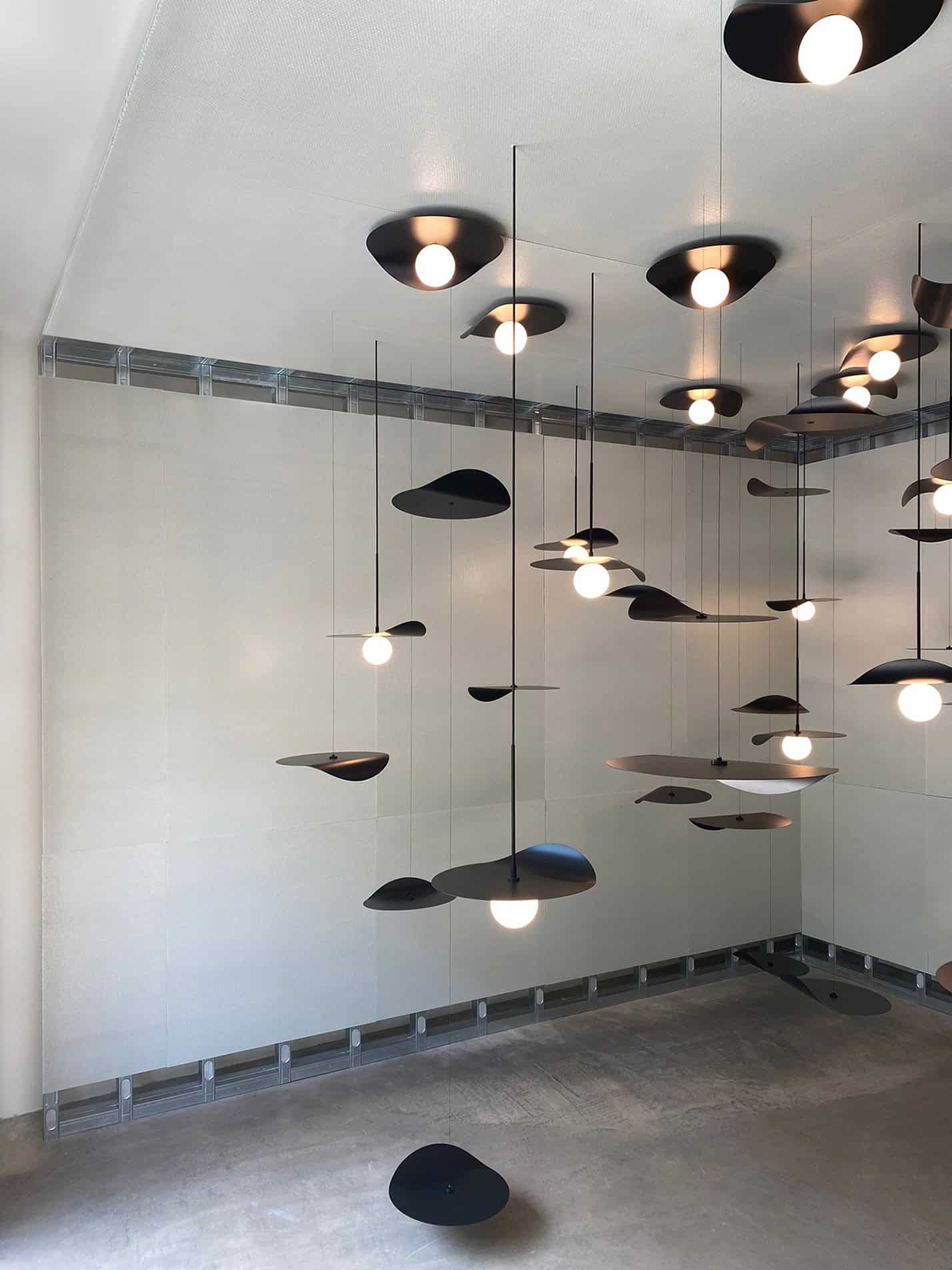 Lampade sospese nere con luci calde, installazione moderna a Milano Design Week 2022.